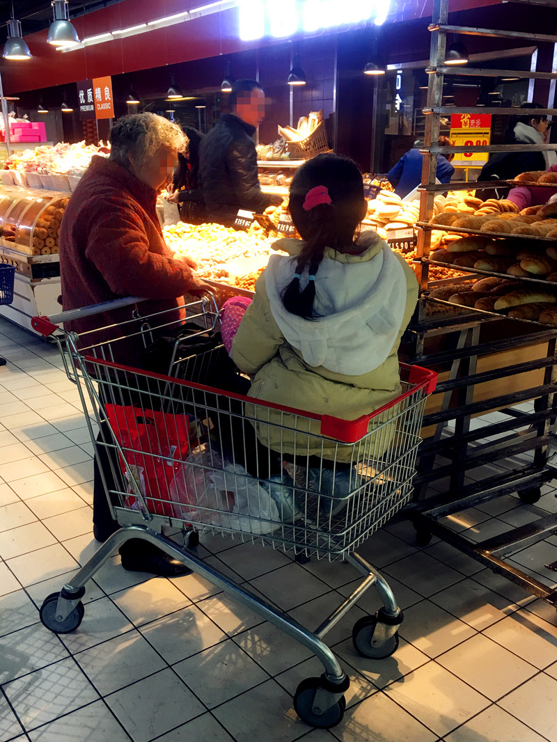 老太推购物车逛超市10岁模样女孩坐其中