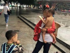 女子穿着外套站在街头  怀里的小孩却赤裸拿着雪糕